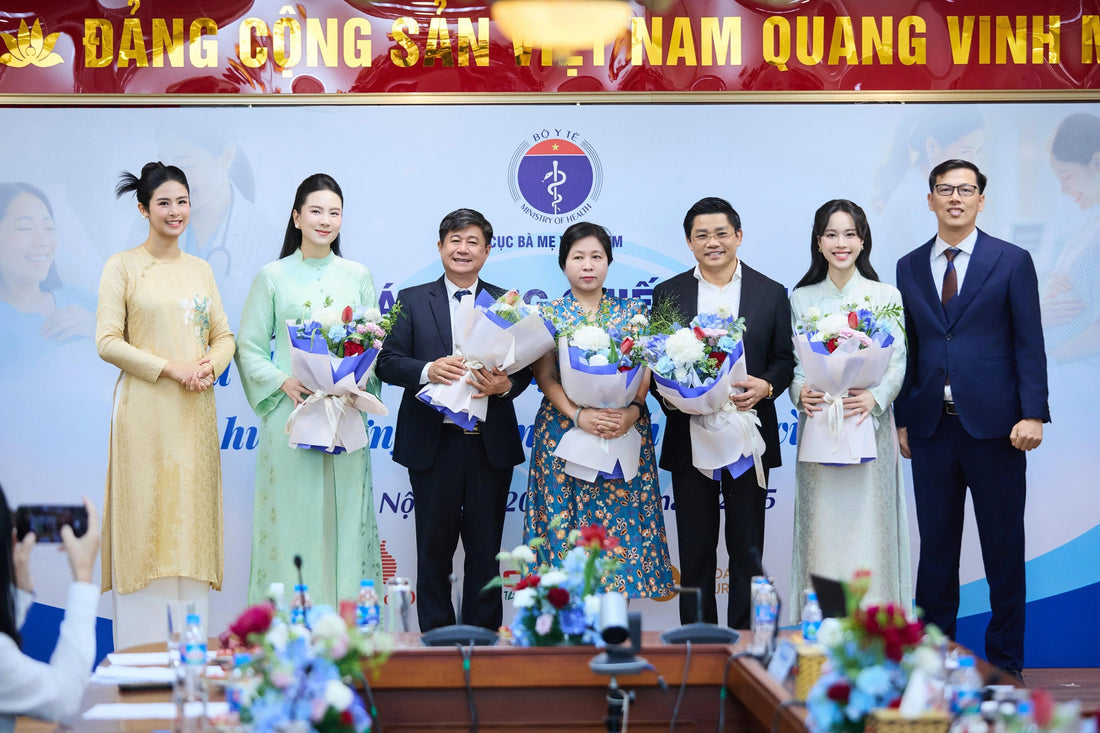 Group photo at Vietnam Ministry of Health event with officials and women in traditional ao dai holding flower bouquets